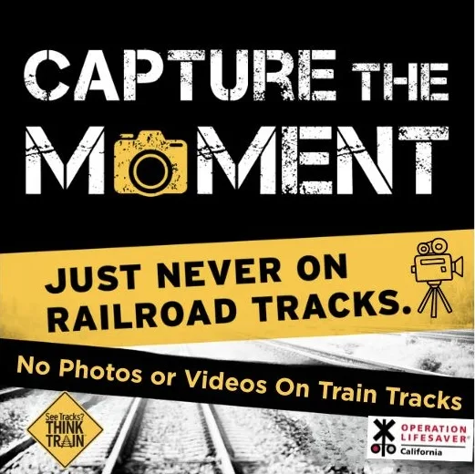 A safety poster says, Capture the moment, just never on railroad tracks. No photos or videos on train tracks, with railroad tracks and logos for safety organizations.